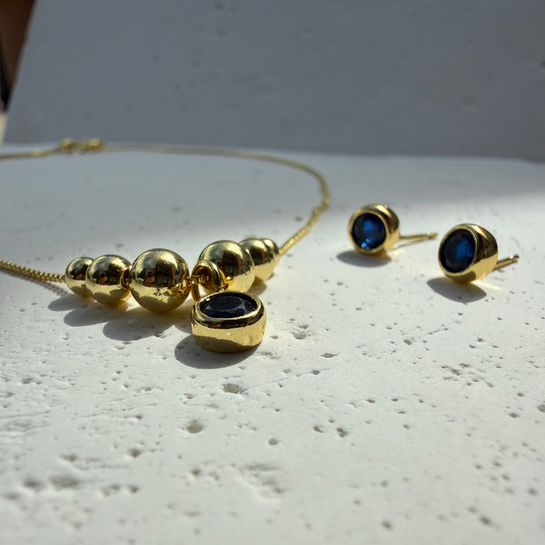 Detalle del dije con piedra sintetica azul y balines dorados en la Cadena Azul Mar